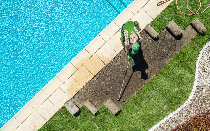 Person landscaping around an in-ground pool.