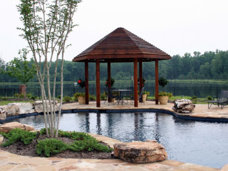 A custom shaped pool with wood arbor gazebo.