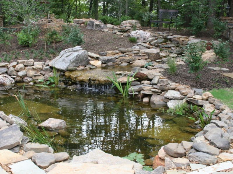 A natural stone stream leading into a lily pad pond.